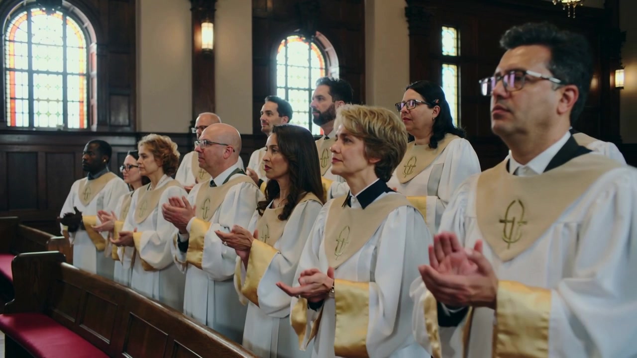 Em resposta ao hino, coro aplaudindo e cantando no banco lateral, vestindo vestes brancas e estolas douradas.