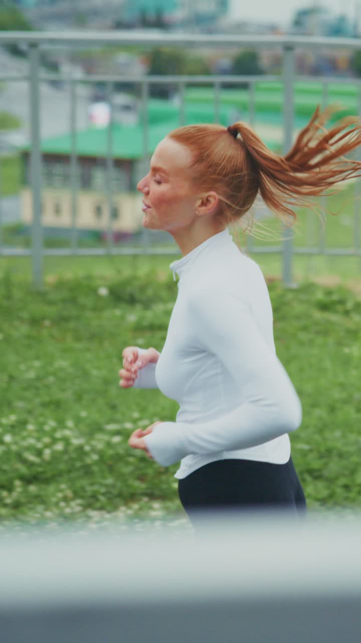 Energetic Young Woman Jogging Outdoors with a Vibrant Smile Amidst Scenic Background of Lush Greenery and Glimpses of a City Landscape