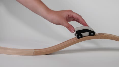 hand moves toy car on wavy wooden track