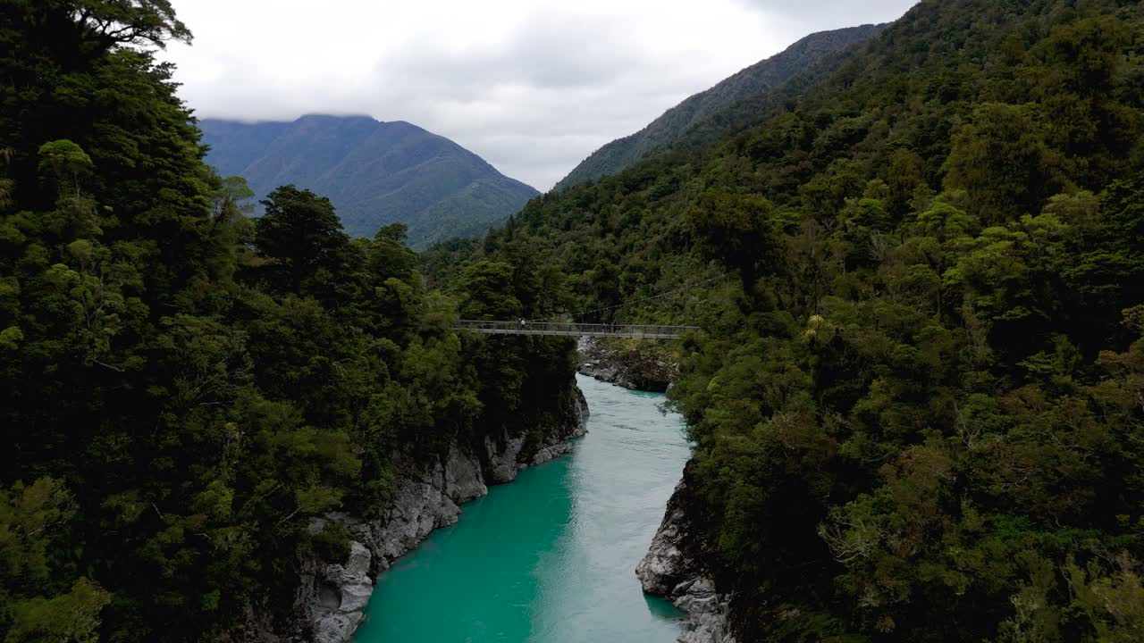Aerial flying down turquoise Hokitika River and Gorge with footbridge. New Zealand