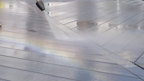 water pressure jet washer cleaning black deck and producing a rainbow with the summer daylight