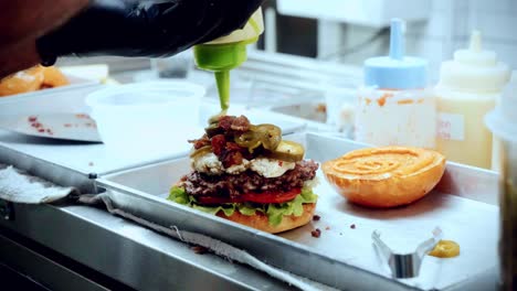 Imágenes-Cinematográficas-De-Cocina-De-Comida-De-4k-De-Un-Chef-Preparando-Y-Haciendo-Una-Deliciosa-Hamburguesa-Casera-En-La-Cocina-De-Un-Restaurante-En-Cámara-Lenta-Poniendo-La-Salsa-Encima-De-La-Hamburguesa-Aplastada