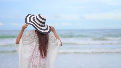 Asiatische-Frau,-Die-Am-Strand-Auf-Das-Meer-Zugeht-Und-Die-Arme-Hochhebt---Rückansicht-Der-Urlaubsvorlage