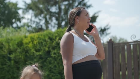 madre embarazada hablando por teléfono con su hija al aire libre