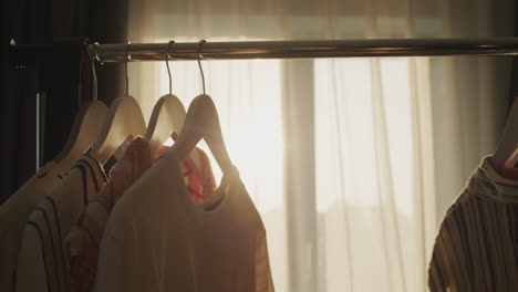 the woman's hands are sorting out the shoulders with dresses in the rays of the setting sun