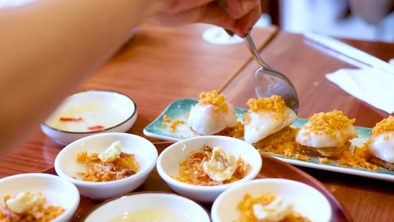 スプーンを使って、小さな白い器に入ったベトナムの蒸し餅をすくう人