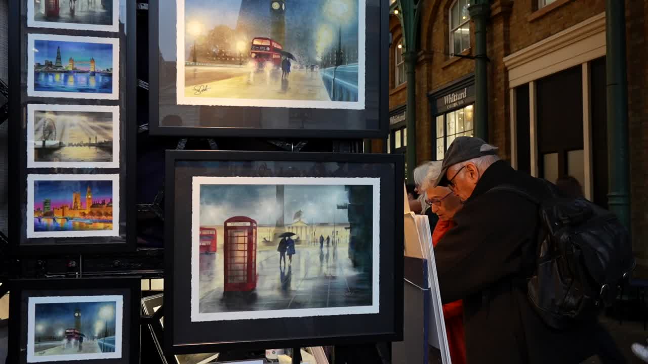 Elderly couple browsing London artwork at Apple Market in Covent Garden during evening