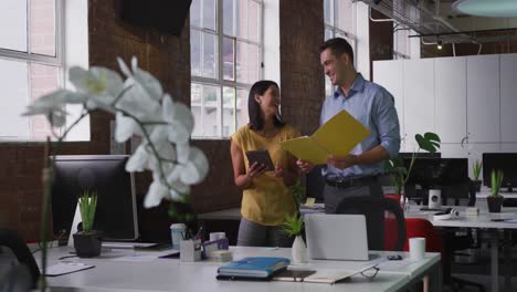 Diverse-male-and-female-business-colleagues-in-discussion-using-tablet-holding-documents-and-smiling