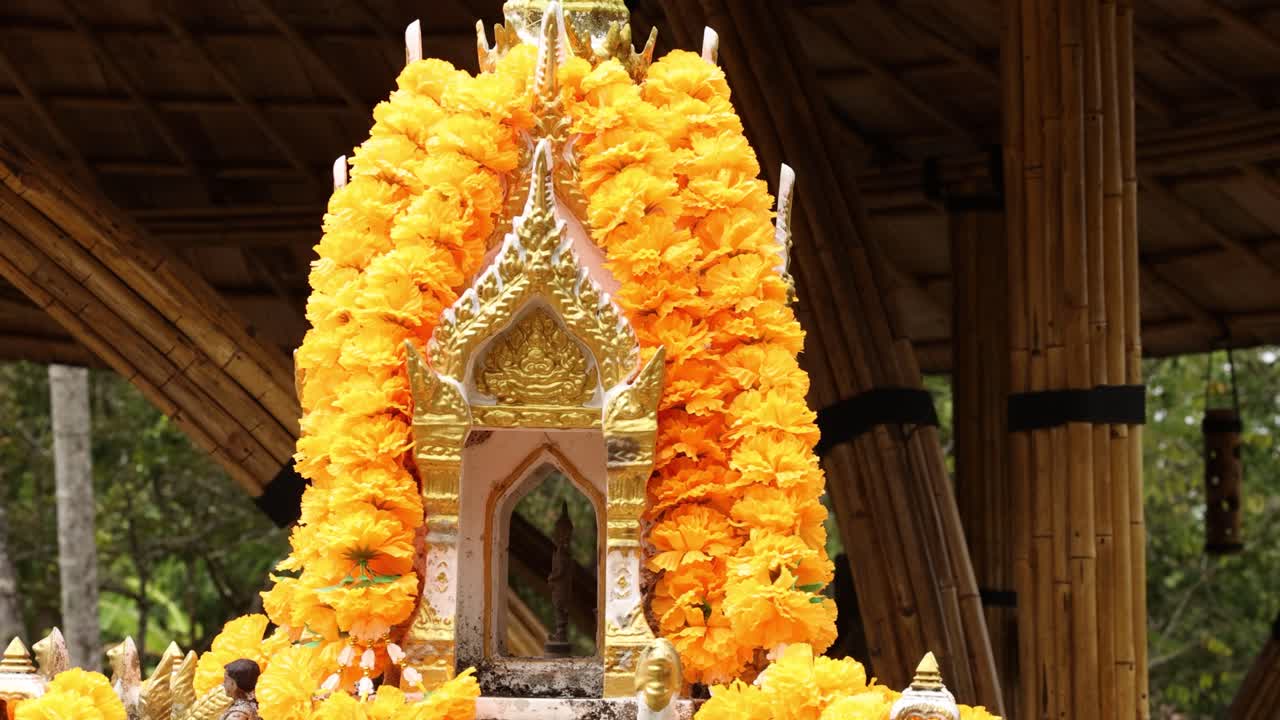una vibrante casa de espíritus tailandeses adornada con guirnaldas de mármol, situada en un entorno tranquilo y estructurado de bambú bajo luz natural