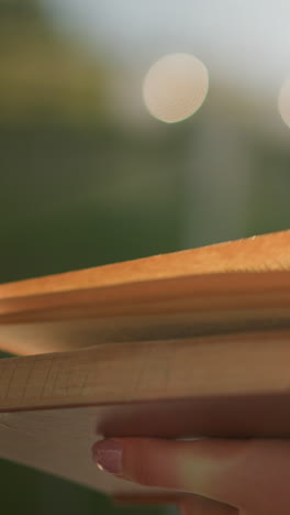 close-up of individual holding book, flipping through pages as sunlight reflects on the person, the blurred background shows two glowing light effects