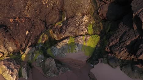 Close-up-shot-of-water-trickling-onto-sandy-beach-from-cliff-rocks-at-sunset-in-Wales