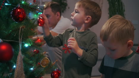 Glückliche-Familie,-Die-Sich-Auf-Das-Feierkonzept-Für-Die-Winterferien-Im-Neuen-Jahr-Vorbereitet.-Ein-Junges-Paar-Aus-Den-30ern-Und-Seine-Bezaubernden-Zwei-Söhne-Im-Vorschulalter,-Die-Den-Weihnachtsbaum-Schmücken,-Schaffen-Eine-Festliche-Stimmungsatmosphäre-In-Einem-Modernen,-Gemütlichen-Haus.-Hochwertiges-4K-Filmmaterial