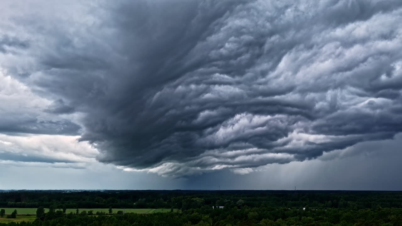 Massive storm cloud system stretches over open green field under dark sky before rainfall begins, twister background