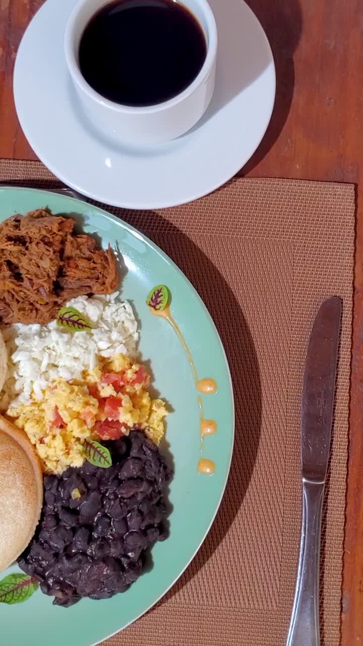 Vertical format — top-down close-up of a Venezuelan creole breakfast served on a wooden table.