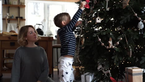 little boy tries to put decorations on the christmas tree