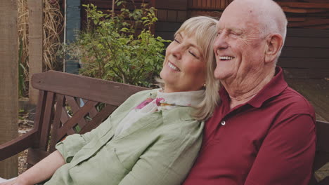 elderly couple laughing together on a bench in the garden