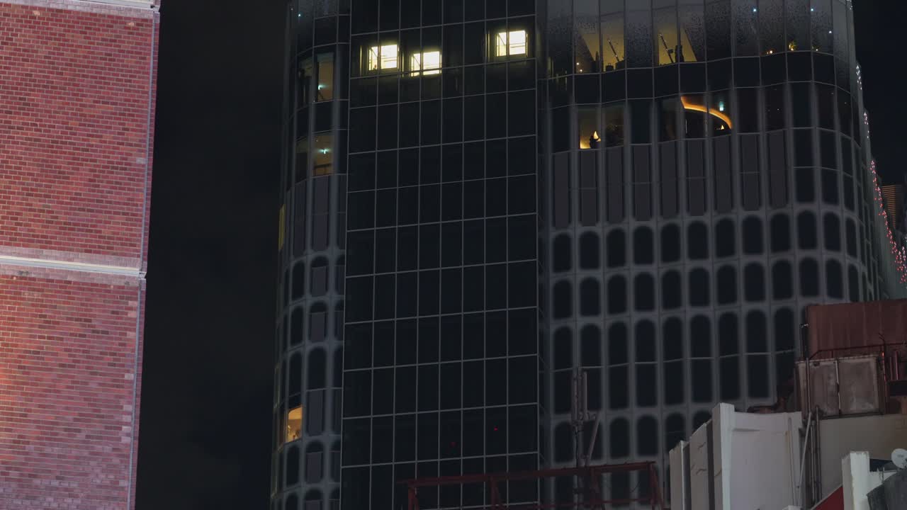 A nighttime street-level view of a modern building with lit-up elevators visibly ascending the building