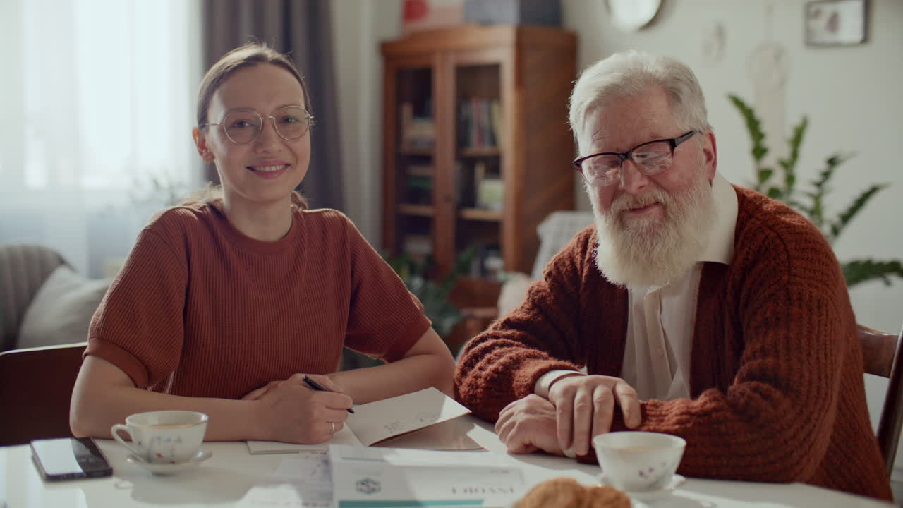 Porträt eines lächelnden älteren Mannes und seiner Enkelin, die mit Rechnungen am Tisch sitzen