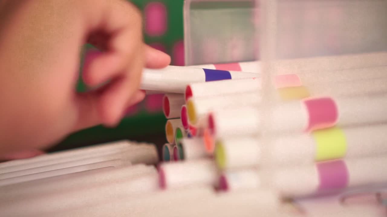 Mano tomando un rotulador de un recipiente, detalle en primer plano, colores vibrantes, materiales de dibujo y proceso creativo.