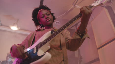 girl playing guitar during a band rehearsal in recording studio