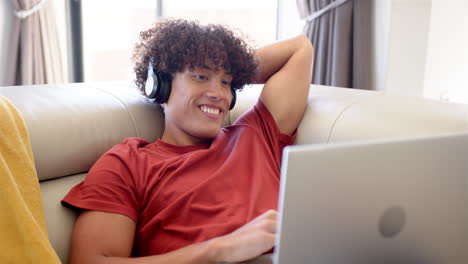 a young biracial man relaxes with his laptop on the couch at home