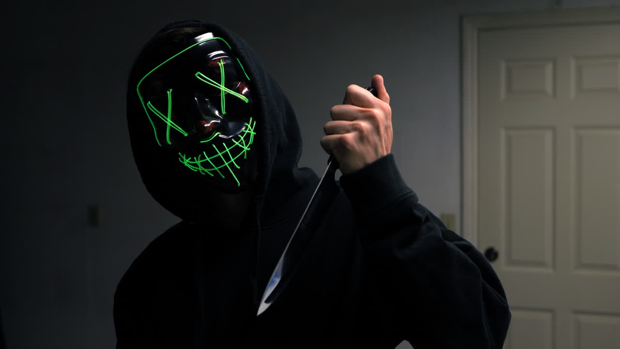 A scary slasher killer in a generic anonymous halloween horror mask pulling a knife on his victim