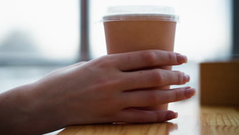 vista lateral de una mujer tocando una taza de café en una mesa de madera brillante con un primer plano de fondo borroso