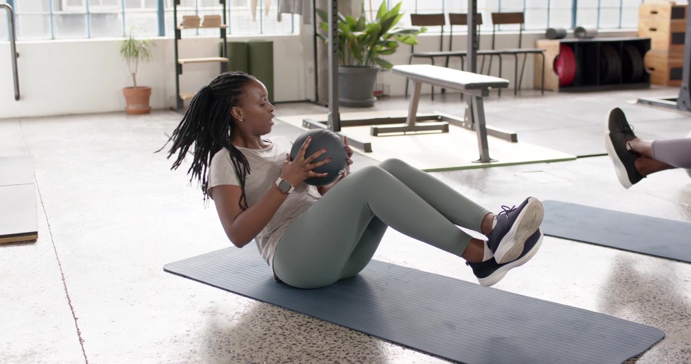 African American women in sportswear holding med ball on mat, rotating torso for core strengthening