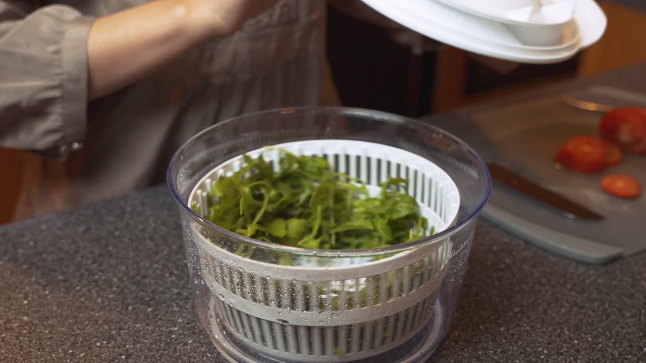 mujer con la mano usando un girador de ensalada para secar verduras de hojas verdes, preparar ensalada para una comida saludable