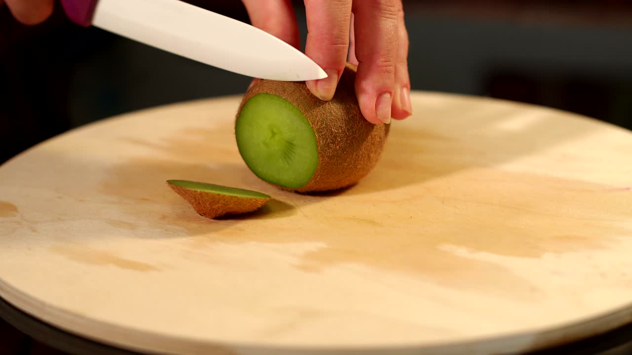 un primer plano de las manos de una mujer cortando kiwi a bordo.