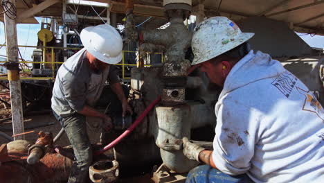 working staff at the drilling site. men in helmets arrange the equipment at oil or gas industry. men using a wrench.