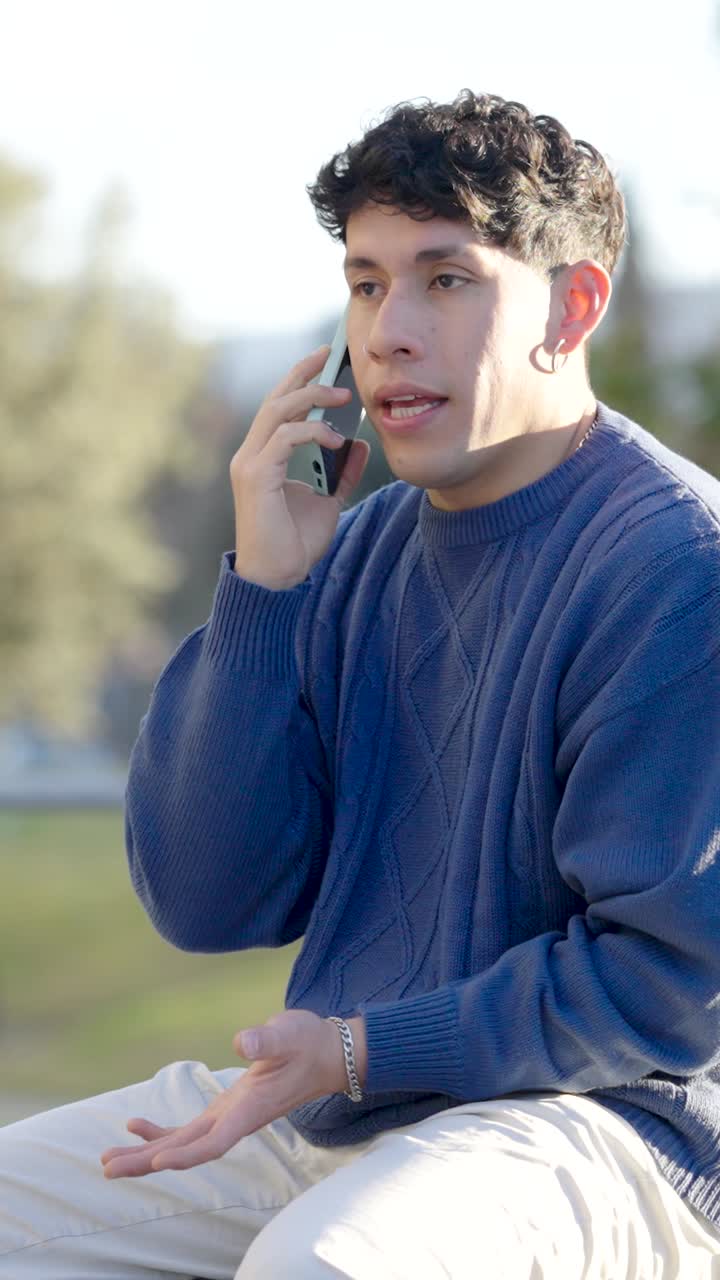 Young man talking on smartphone in park. Vertical