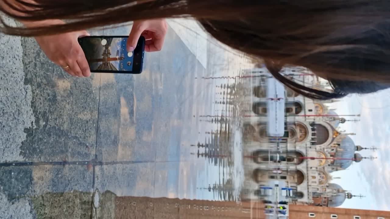 mujer viajera joven tomando imágenes de reflejo de la basílica de san marco durante el período acqua alta, vertical