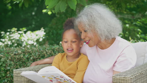 grandmother sitting outdoors in garden with granddaughter at home reading book together