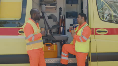 Two-Medical-Assistances-Talking-And-Drinking-Coffee-Outside-The-Ambulance