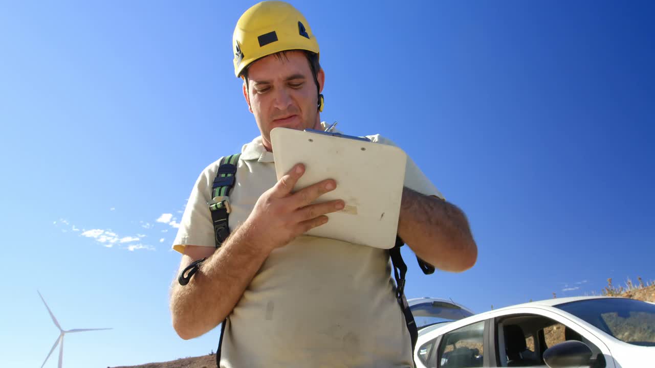 ingeniero masculino escribiendo en el clipboard en el parque eólico 4k