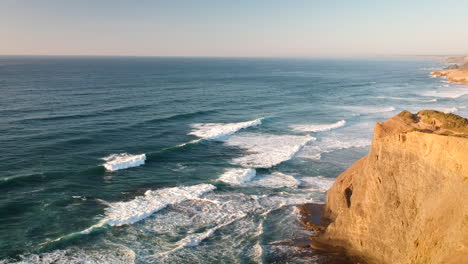 aerial drone shot of waves hitting a beach with cliffs during a sunset in southern portugal