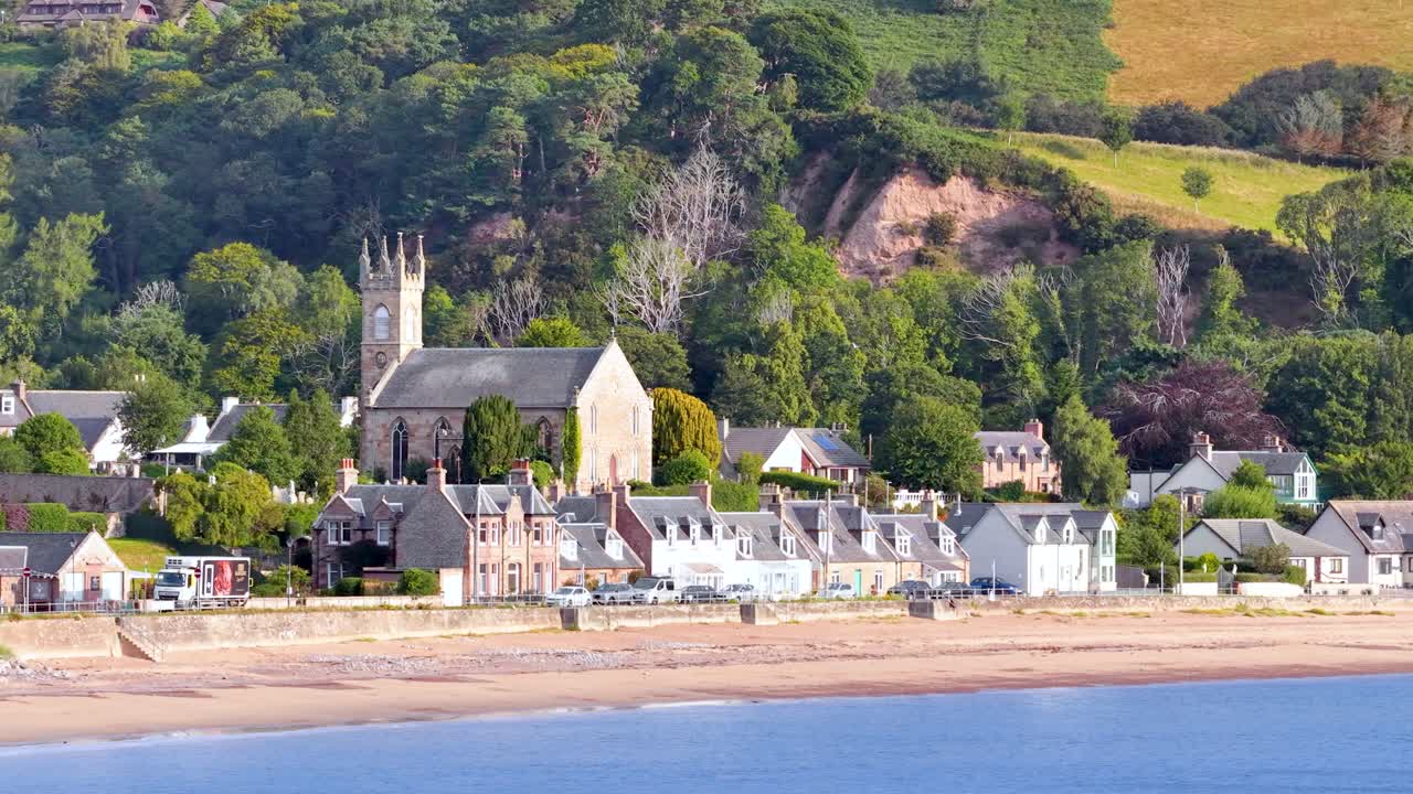 Daytime telephoto pan reveals Rosemarkie village, church, graveyard, and lush Highland landscape