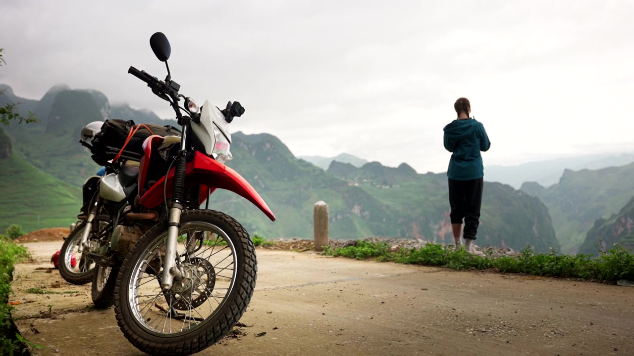 Turista donna vicino a una moto si gode la vista da un punto panoramico di montagna, Ha Giang Loop