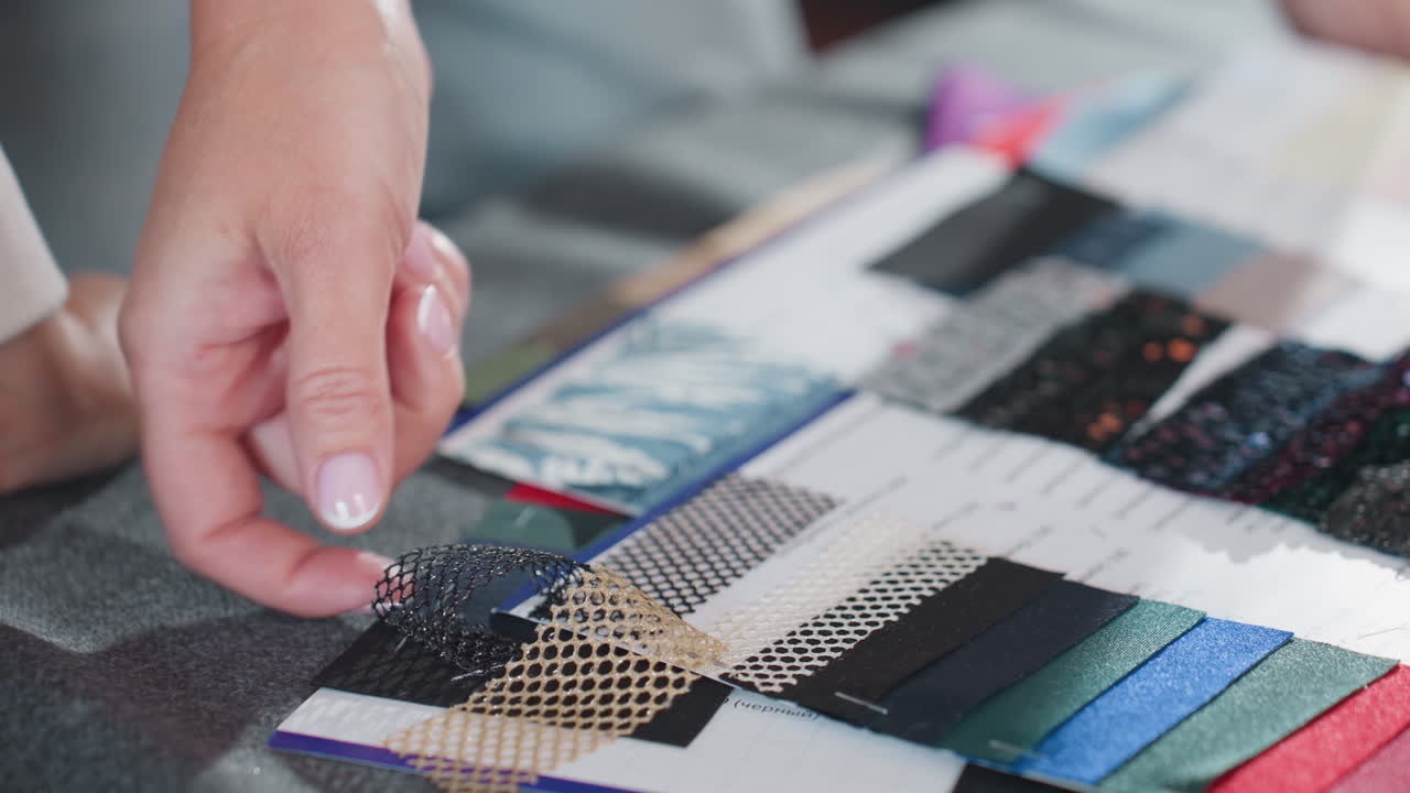 Close up of female hand pointing and lifting colorful net and lace material samples from creative fashion design swatch book, showcasing intricate patterns, and fabric selection process