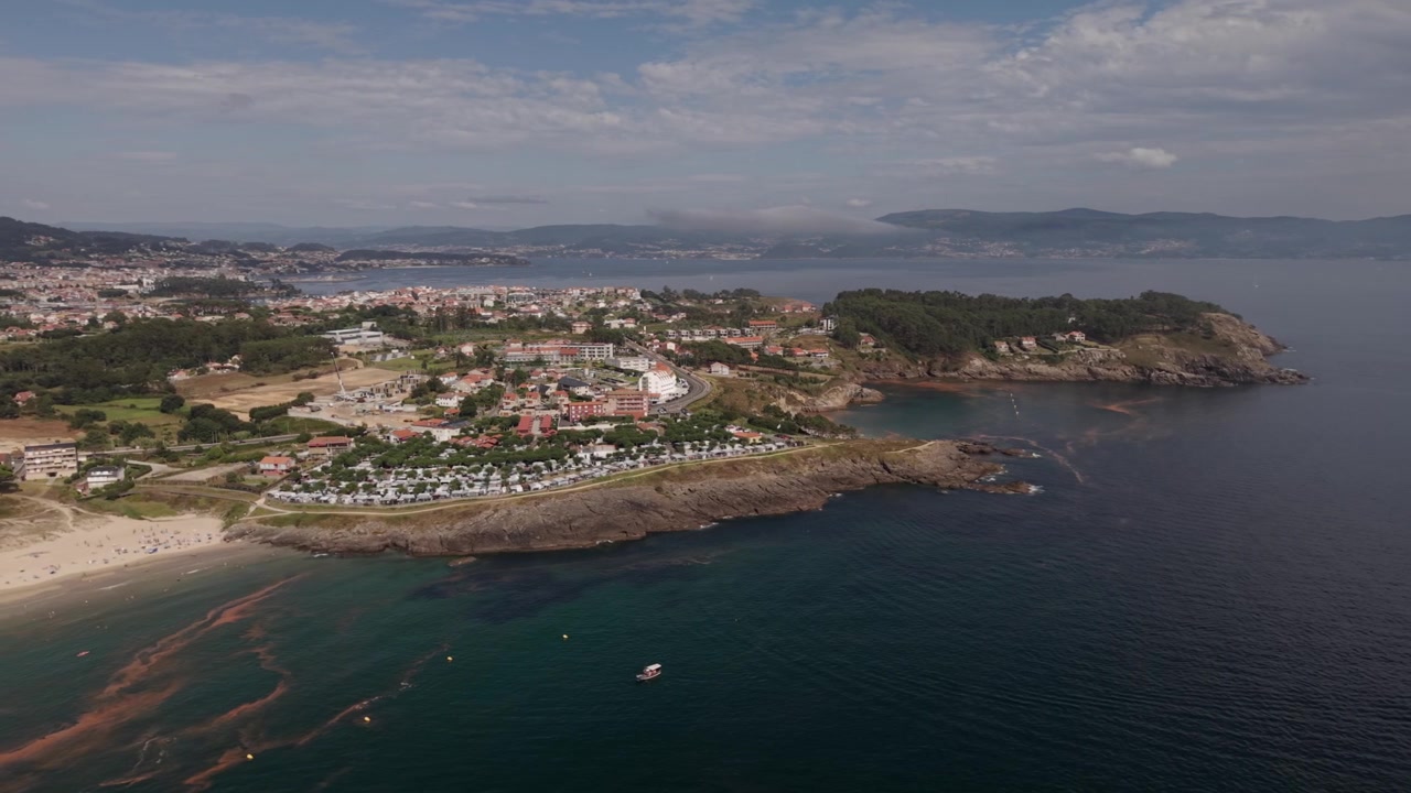 Vista aerea rotante con drone del promontorio della baia di Montalvo con un campeggio, boschi verdi, costa rocciosa e acqua turchese a Sanxenxo, Galizia, Spagna.