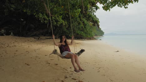 a woman swings on a wooden swing on a beautiful tropical beach in thailand