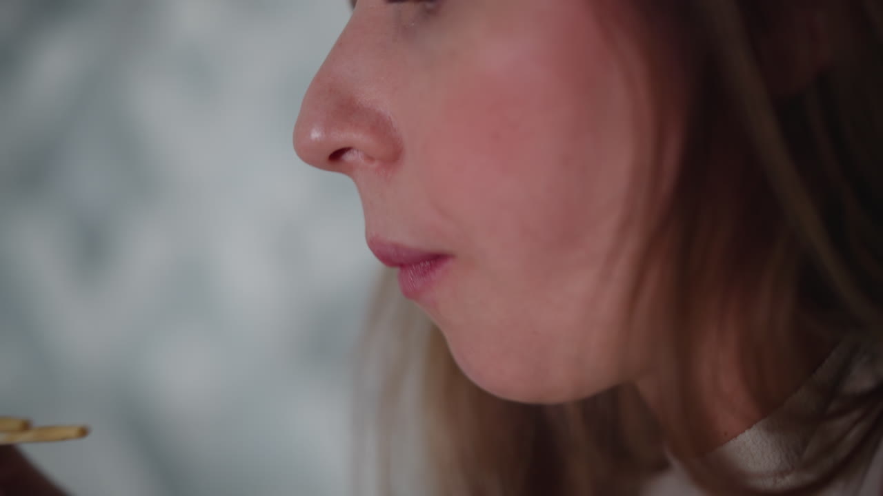 Close up of girl with painted lips gently licking chopsticks after eating, focused on mouth and soft facial features, side profile shot with natural lighting and calm background