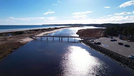 flyover of footbridge and coastal river into blue sky and reflections over waters of a coastal river