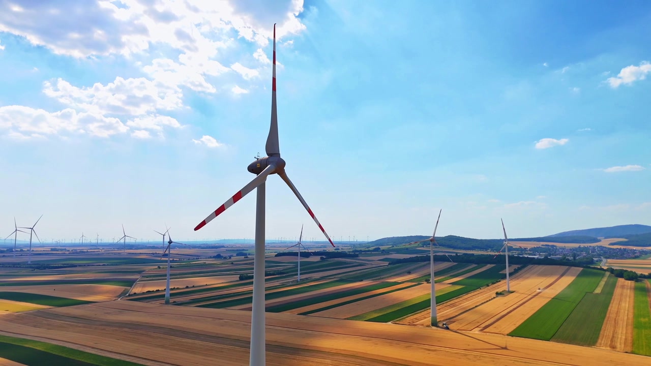 Close aerial view of wind turbine blade tip. Blade with red safety marking, drone shot, fields visible below