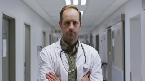 portrait of caucasian male doctor with arms crossed standing in the corridor at hospital