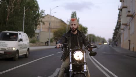 motociclista barbudo conduce una bicicleta en la ciudad, esperando el semáforo, sonriendo