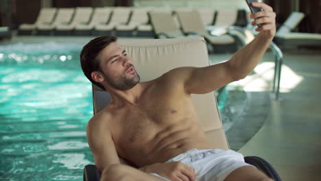 hombre de primer plano divirtiéndose cerca de la piscina cubierta. hombre haciendo una selfie en el teléfono móvil