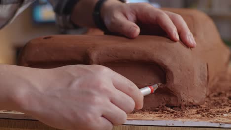 close up of man automotive designer's hands using spatula to smooth out the surface and create details in the sculpture of car clay in the studio