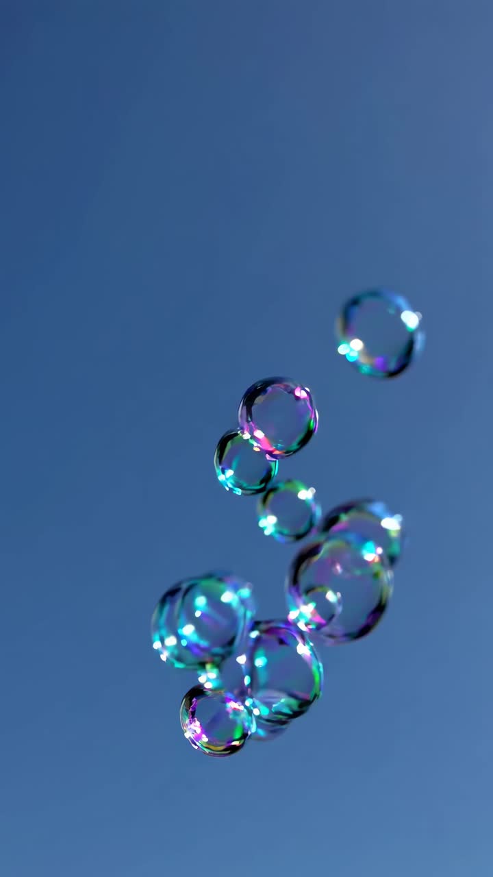 A video captures colorful soap bubbles floating against a clear blue sky, shot from a low angle